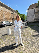 A person stands against a plain background, wearing a Marble Print Short Sleeve Cropped Jacket by Maison Lilli. She also wear a gold hoop earrings, and a thick gold chain necklace.