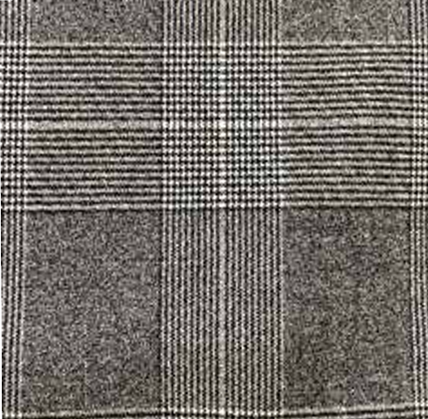 A person is wearing high-waisted, gray wool-blend Paperbag Pleated Pants - Glen Plaid by Maison Lilli with a large belt buckle. They have one hand in their pocket and are also wearing a loose-fitting short-sleeved off-white top and black heels. The background is plain light gray.